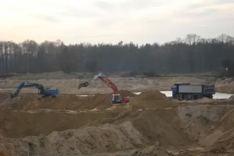 Koparki i wywrotka pracują na placu budowy, wykonując prace ziemne.