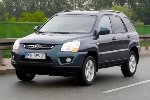 Ciemnoszary Kia Sportage 2008 na drodze, z zielonym ogrodzeniem w tle.