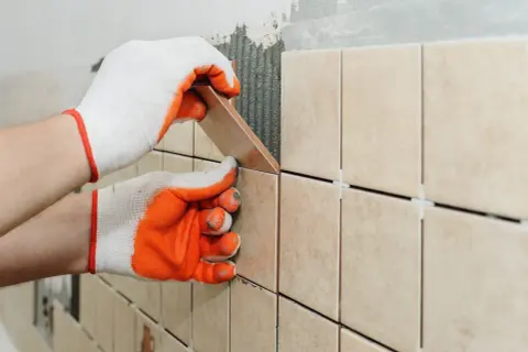 Hands in gloves carefully place a tile, demonstrating how to tile a shower floor.