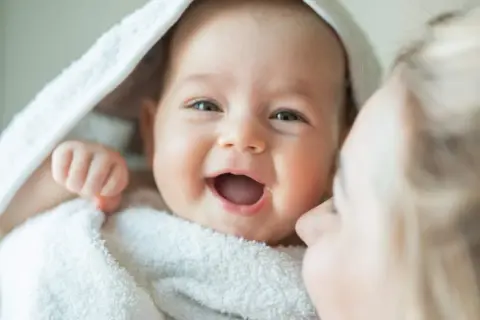 La alegría contagiosa cuando empieza a reírse un bebé, envuelto en una toalla blanca, con una madre dándole un beso.