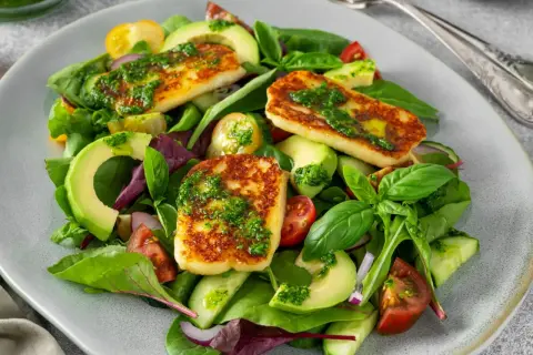 Pyszna sałatka z halloumi, awokado, pomidorkami i ogórkiem, polana zielonym sosem.