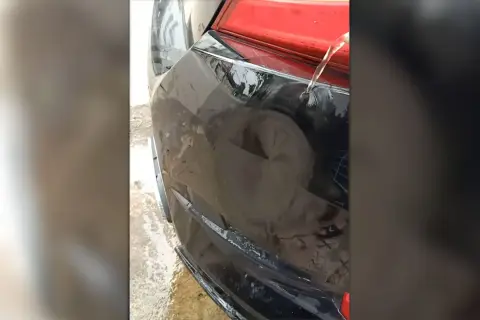 Usuwanie wgnieceń gorącą wodą na czarnym zderzaku samochodu. Woda spływa po uszkodzonym fragmencie.