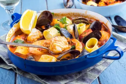 Caldereta de pescado humeante en cazuela azul, con gambas, mejillones, trozos de pescado blanco y limón.