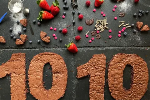 Zahlentorte mit Biskuitboden in Form einer 10, dekoriert mit Erdbeeren, Blaubeeren und Schokoladenherzen.