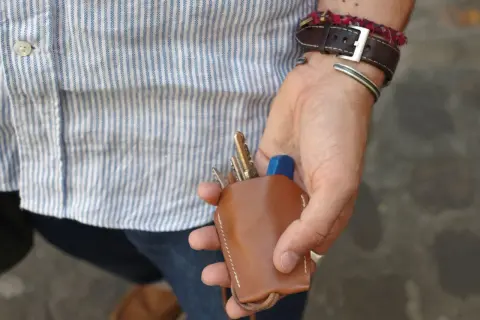 Main d'un homme au style workwear, tenant un étui à clés en cuir marron.