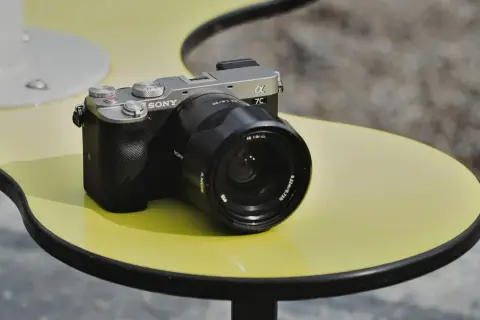 Srebrno-czarny aparat Sony a7c z obiektywem na żółtym stoliku.