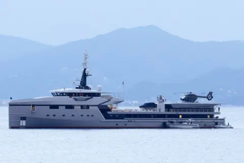 Lo yacht Koru, con il suo elicottero pronto al decollo, naviga maestoso in acque tranquille, con le montagne sullo sfondo.