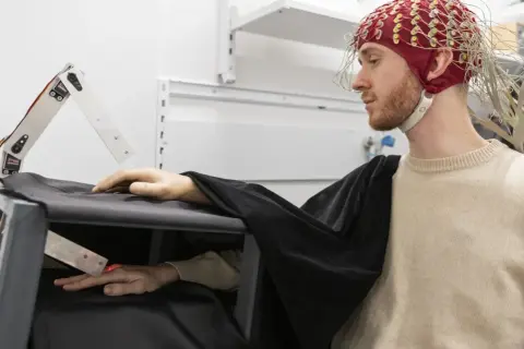 Joel Svenningsson med EEG-hjälm och en robotarm som interagerar med hans hand.