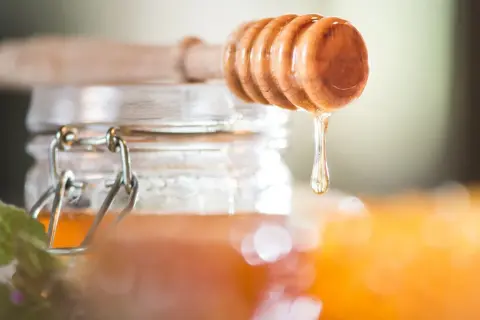 Ein Holzlöffel tropft goldenen Akazienhonig in ein Glas. Dieser Honig ist nicht nur süß, sondern auch gesund.