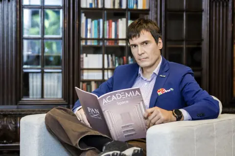 Mężczyzna w niebieskiej marynarce siedzi w fotelu i czyta czasopismo "Academia".
