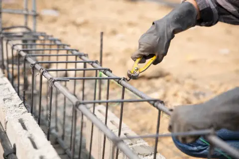 Manos enguantadas atando varillas de acero para como hacer los cimientos de una casa.