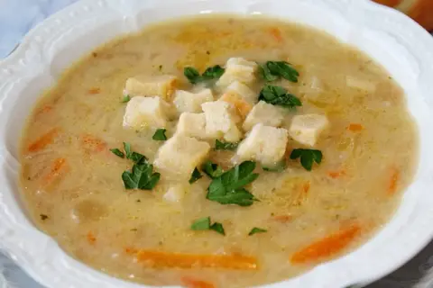 Aksamitna zupa cebulowa z grzankami i natką pietruszki, podana w białej misce.