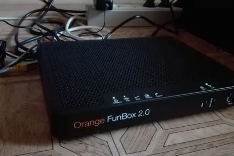 Czarny router Orange FunBox 2.0 z wieloma kablami podłączonymi do listwy zasilającej.