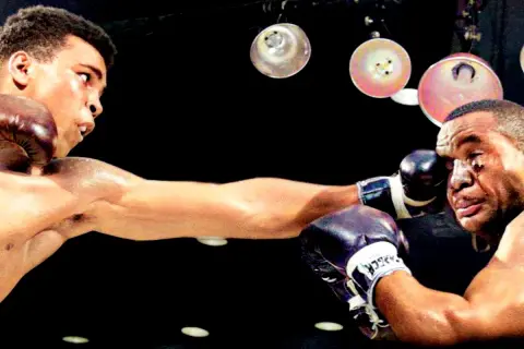 Cassius Clay, som Muhammad Ali, levererar en kraftfull högerkrok mot sin motståndare i en intensiv boxningsmatch.