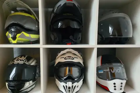 Sześć kasków motocyklowych różnych marek i stylów, ułożonych w białych przegrodach.