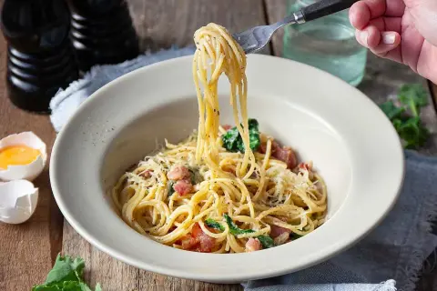 En gaffel lyfter en portion krämig spaghetti carbonara från en skål. Ett perfekt pasta carbonara recept för en god middag.
