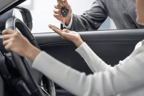 Kluczyki do nowego auta przekazuje sprzedawca, a klientka zastanawia się: leasing czy gotówka?