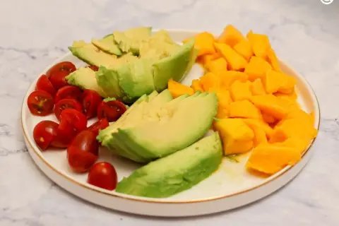 Plato con ensalada de mango y aguacate, tomates cherry cortados por la mitad y aguacate en láminas.