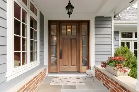 A beautiful front door makeover featuring a warm wooden door with glass panels, flanked by windows. A bird-themed doormat welcomes guests.