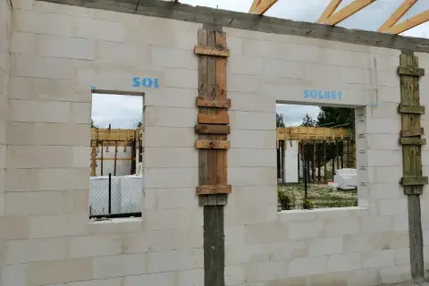 Ściana z bloczków z otworami okiennymi i drewnianymi szalunkami, w trakcie budowy.