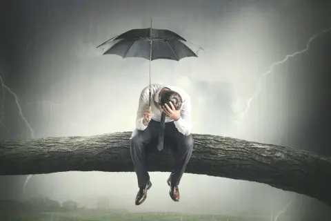 Uomo seduto su un ramo d'albero sotto un temporale, con un ombrello. Sembra che il mio ragazzo è depresso, perso nei suoi pensieri.