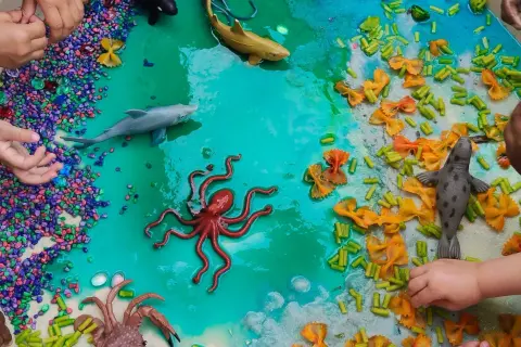 Ocean-themed sensory bin with toy sea creatures, colorful pebbles, and pasta provides engaging sensory activities for 1 year olds.