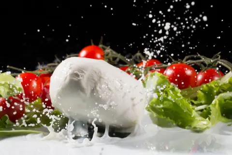 La mozzarella fresca, circondata da pomodorini e lattuga, viene spruzzata con latte in un movimento dinamico.