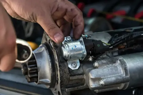 Mechanik naprawia rozrusznik w aucie, przykręcając śrubę.