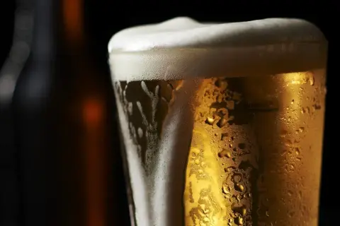 Bicchiere di birra olandese dorata con schiuma bianca e goccioline di condensa, su sfondo scuro.