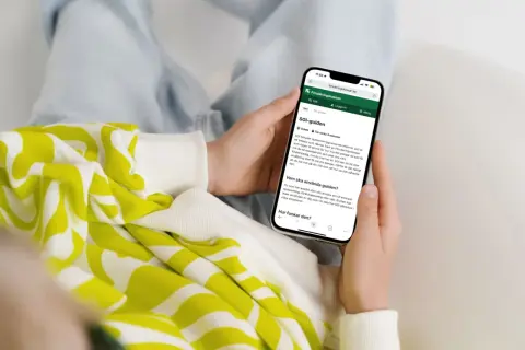Person håller upp en mobiltelefon som visar Försäkringskassans SGI-guide. Guiden förklarar vad SGI är och hur den fungerar för enskild firma.