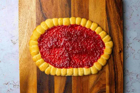 Pyszny mazurek pistacjowy z malinami, ozdobiony delikatnymi ciasteczkami, kusi swoim wyglądem.