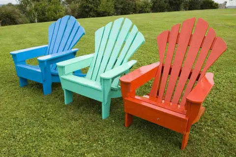 Tres sillas de madera de estilo Adirondack, pintadas de azul, verde menta y naranja, listas para disfrutar del exterior. ¡Pintar sillas de madera sin lijar es fácil!