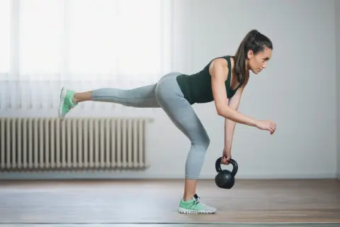 Woman performing kettlebell balance exercises, balancing on one leg while holding a kettlebell.