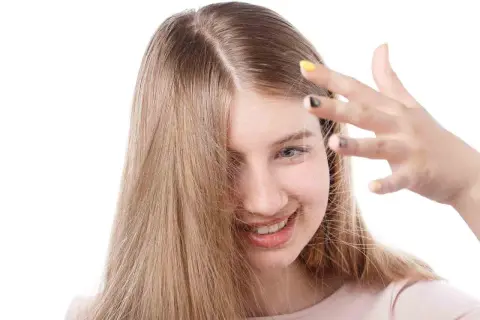 Chica sonriente con cabello rubio que se electrifica. Descubre cómo quitar la electricidad del pelo para un look suave.