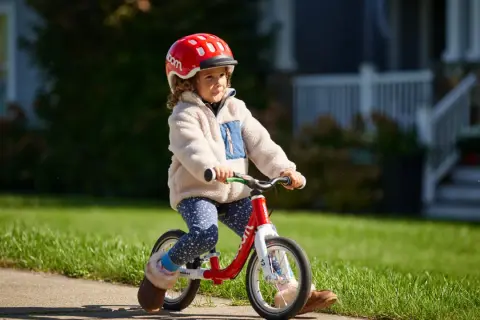 Kleines Kind mit Helm fährt Laufrad. Die richtige Einstellung des Laufrads ist wichtig für den Fahrspaß.