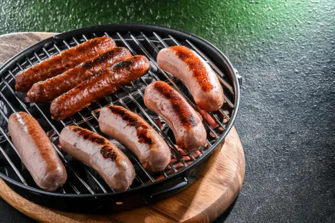 Mehrere rohe Bratwürste braten auf einem Grill. Sie sind noch nicht ganz durch, aber schon schön gebräunt.