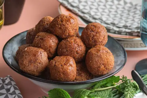Un piatto pieno di polpette di fagioli dorate, guarnite con erbe fresche.