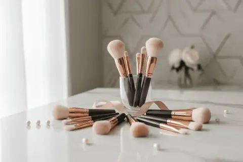 Un ensemble de pinceaux de maquillage aux manches noirs et dorés, disposés en cercle sur une table marbrée. Un ruban rose pâle les entoure, rappelant l'importance de nettoyer pinceau maquillage pour une peau saine.