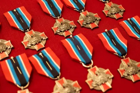 Kolekcja medali i odznaczeń OSP z orłem i czerwono-niebiesko-czarnymi wstążkami, ułożona na czerwonym tle.