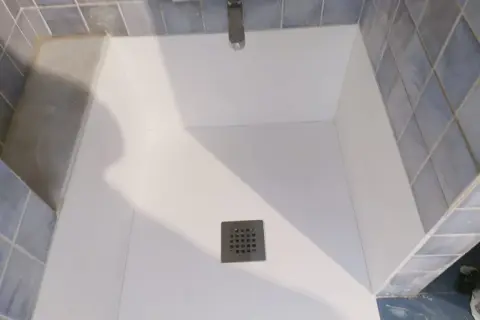 Instalación de un nuevo plato de ducha blanco, con azulejos azules y grifería cromada.