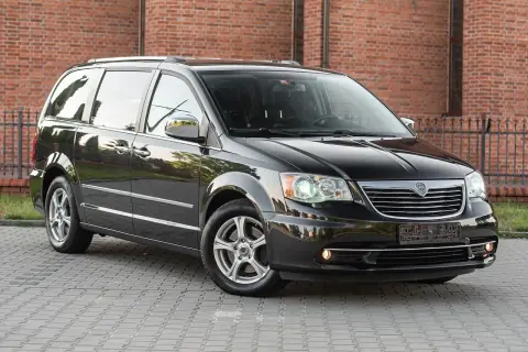 Czarny Lancia Voyager stoi na brukowanym podjeździe przed ceglanym budynkiem.