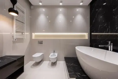 Baño moderno con bañera exenta, inodoro, bidet y toallero. Iluminación indirecta crea un ambiente chill out.