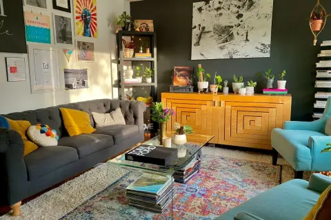 Salon w stylu maksymalistycznym: szara sofa, turkusowe fotele, kolorowy dywan, mnóstwo roślin i dekoracji na ścianach.