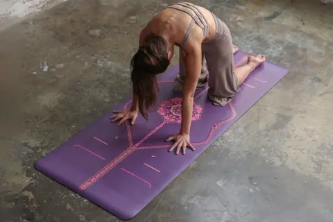 Mujer en postura de la esfinge sobre una esterilla de yoga morada con diseño.