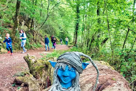 Un duende azul vigila las rutas con niños en Asturias. Familias disfrutan del sendero boscoso.