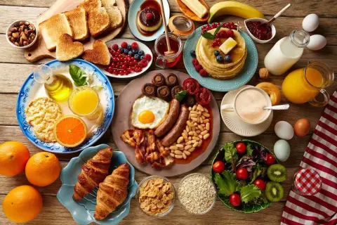Un copieux repas sportif : œufs, saucisses, haricots, toasts, fruits, pancakes, croissants, café et jus d'orange.