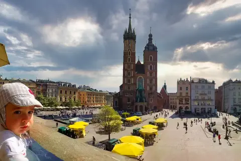 Małe dziecko w czapce z daszkiem patrzy na Rynek Główny w Krakowie. W tle Bazylika Mariacka i kolorowe kamienice.