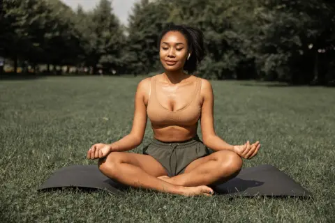 Femme méditant en plein air, une posture de yoga pour maigrir. Elle est assise sur un tapis dans l'herbe, les yeux fermés, en pleine concentration.