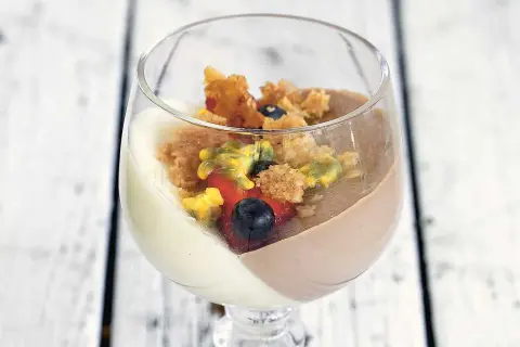 En vacker pannacotta tårta i glas med bär och smulor.