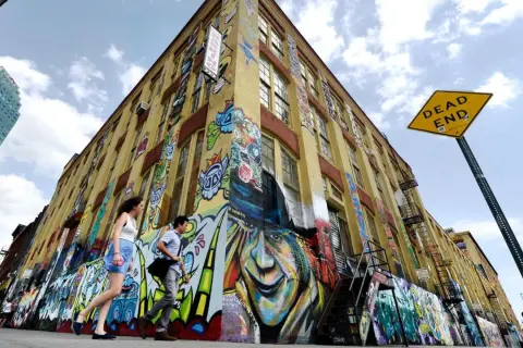 Gelbes Gebäude mit Graffiti-Kunst, Menschen gehen vorbei, "DEAD END"-Schild.